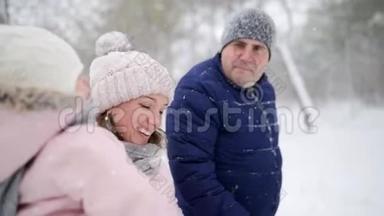 友好的全家人在降雪的情况下在冬天的森林里散步。 父亲、母亲和女儿